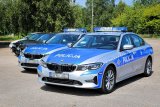 Zdjęcie przedstawia pięć radiowozów marki BMW ustawionych bokiem na parkingu. Dwa pierwsze są oznakowane napisami Policja. Za nimi ustawione są trzy nieoznakowane pojazdy marki BMW.