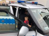 na zdjęciu widać oznakowany radiowóz policyjny marki Skoda. Pojazd ma otwarte wszystkie drzwi. Wewnątrz siedzą dzieci.