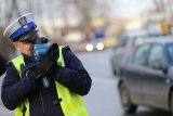 zdjęcie przedstawia umundurowanego policjanta, który miernikiem prędkości mierzy prędkość przejeżdżających pojazdów