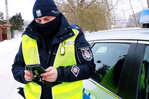 Policjant w mundurze stoi, trzyma urządzenie mobilne