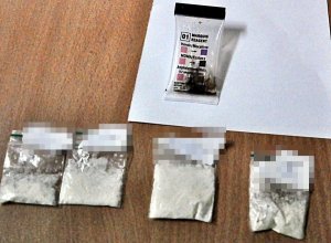 Cztery torebki foliowe wypełnione białym proszkiem leżą na stole, obok nich leży tester narkotykowy.