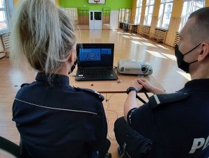Policjant w mundurze i policjantka w mundurze siedzą przed laptopem.