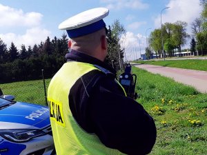 Policjant w mundurze stoi przy drodze, trzyma ręczny miernik prędkości