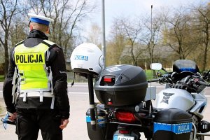Policiant w mundurze stoi na świeżym powietrzu, obok stoi motocykl