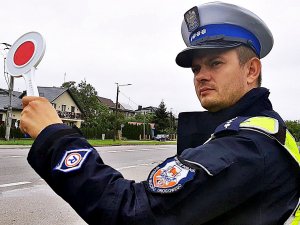 Policjant w mundurze stoi, trzyma tarcze do zatrzymywania pojazdów.