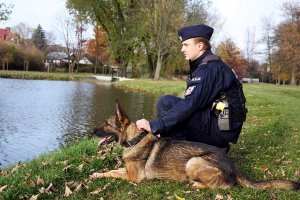 Policjant w mundurze z psem siedzą nad stawem.