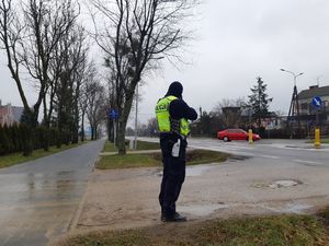 Policjant stoi przy drodze i trzyma miernik prędkości.
