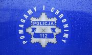 Na niebieskim tle napis: &quot;POLICJA 112 POMAGAMY I CHRONIMY&quot; oraz odznaka policyjna.