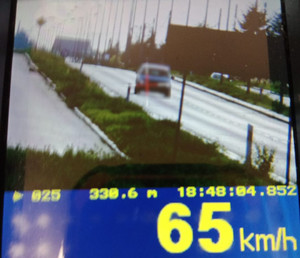 Zdjęcie z miernika prędkości, widać jadący samochód i wyświetloną jego prędkość 65 km/h.