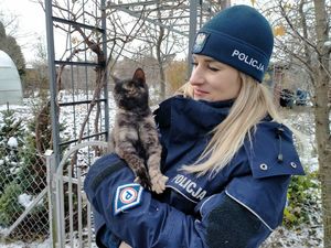 Policjantka stoi zimą, trzyma kota.
