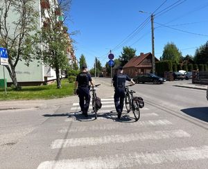 Dwóch umundurowanych policjantów z rowerami przechodzi przez przejście dla pieszych