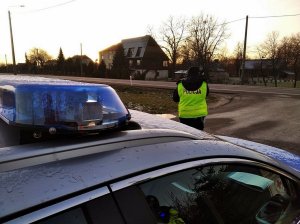 Policjant stoi przy drodze, obok stoi radiowóz