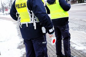 Dwaj policjanci stoją przy drodze, jeden trzyma w reku tarczkę do zatrzymywania pojazdów