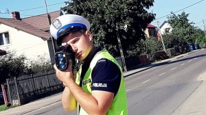 Policjant w mundurze stoi przy drodze i trzyma ręczny miernik prękości