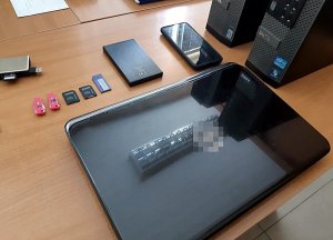 Na biurku leży laptop, dwa telefony komórkowe, karty SIM.