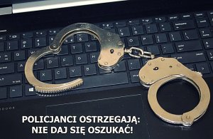 Klawiatura komputera, na niej leżą kajdanki, napis&quot;POLICJANCI OSTRZEGAJĄ NIE DAJ SIĘ OSZUKAĆ&quot;.