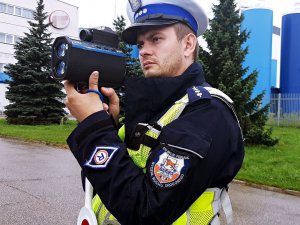 Policjant stoi na świeżym powietrzy, trzyma ręczny miernik prędkości.