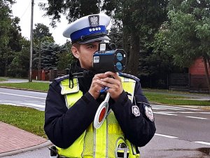 Policjant w mundurze stoi, trzyma miernik prędkości.