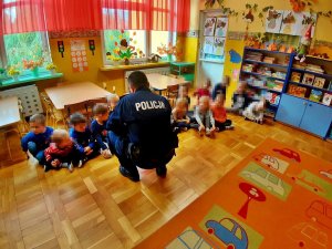 W sali siedzą dzieci, obok nich jest policjant w mundurze.