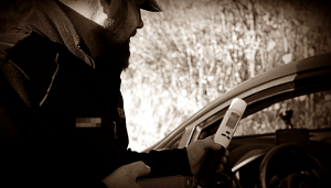 Policjant stoi przy samochodzie, trzyma miernik prędkości.