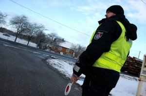 Policjant w mundurze stoi przy drodze, trzyma tarczkę do zatrzymywania pojazdów.