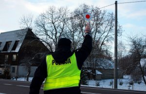 Policjant w mundurze podnosi do góry tarczę do zatrzymywania pojazdów.