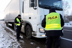 Dwaj policjanci w mundurach stoją przy samochodzie ciężarowym.