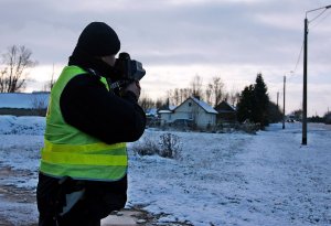 Policjant w mundurze stoi przy drodze, trzyma miernik prędkości.