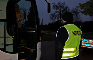 Policjant w mundurze stoi na świeżym powietrzu, przed nim stoi autokar.