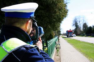 Policjant stoi przy drodze, trzyma miernik prędkości.