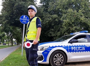 Policjant w mundurze stoi przy drodze, trzyma tarcze do zatrzymywania poajzdów.