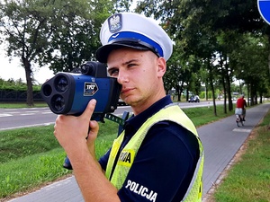 Policjant w mundurze stoi na świeżym powietrzu, trzyma miernik prędkości.