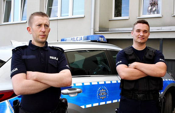 Dwaj policjanci stoją przy radiowozie.