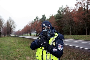 Policjant z miernikiem prędkości stoi przy drodze.