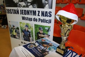 Na stole leżą plakaty z wizerunkiem policjantów, obok stoi puchar z nałozona czapką Mikołaja.