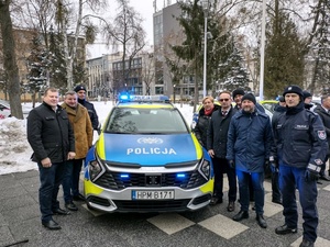 Osoby stoją przy radiowozie.