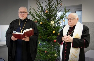 Księża stoją w budynku przy choince.