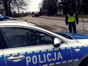 Policjant w mundurze i radiowóz stoja przy drodze.