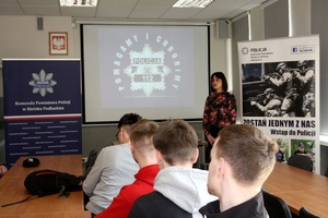 Osoby siedza w budynku, na wyświetlaczu widać napis POLICJA 112 Pomagamy i chronimy.