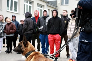 Osoby i policyjny pies stoją na placu komendy.