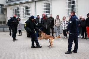 Policjant i osoby stoją na placu komendy.