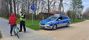 Policjant w mundurze i radiowóz stoją przy drodze.