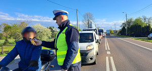 Droga, policjant stoi przy motocykliście i trzyma urządzenie do pomiaru stanu trzeźwości.