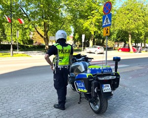 Umundurowany policjant stoi przy motorze w rejonie przejścia dla pieszych