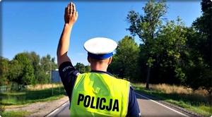 Policjant na drodze podnosi rękę do góry.