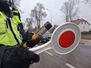 Policjant trzyma tarczkę do zatrzymywania pojazdów i urządzenie alco blow.