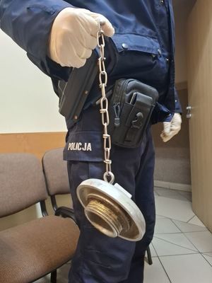 Policjant trzyma metalową nasadę od hydrantu.