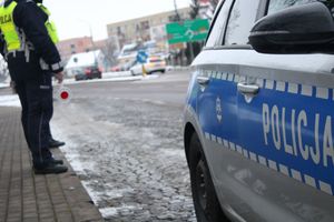 Policjant zimą stoi przy drodze.