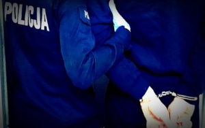 Policjant trzyma osobę, która ma załozone na ręce kajdanki.