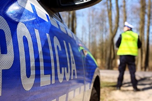 Policjant i radiowóz stoja przy drodze.